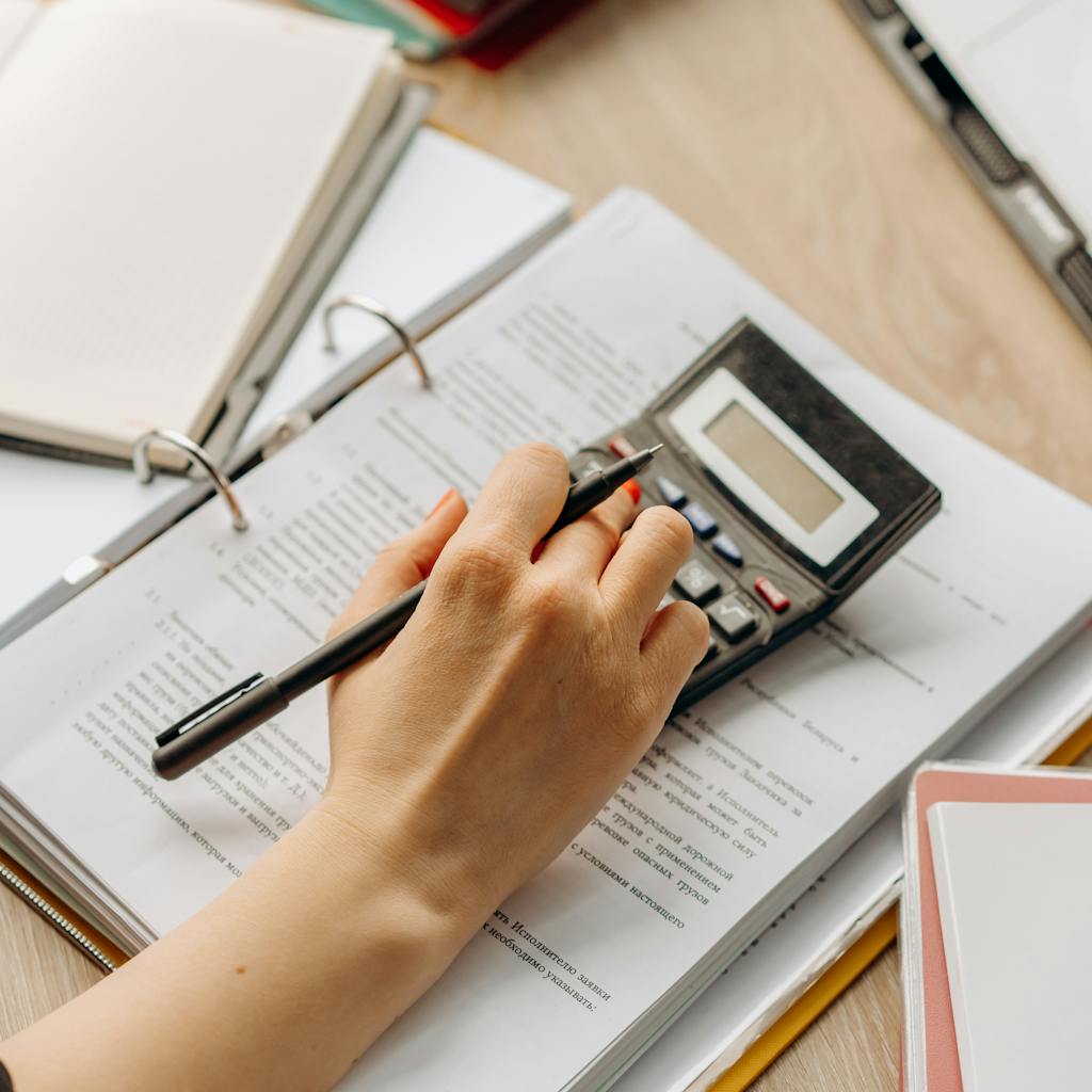 Close-up of a hand using a calculator on documents in an office setting.